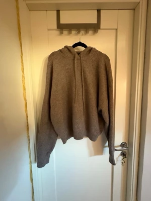 Beige hoodie i mjukt material - En beige hoodie med avslappnad passform och stor huva. Tillverkad i ett mjukt, stickat material som känns skönt mot huden. Perfekt för dig som gillar en enkel och stilren look. Hoodien har långa ärmar och ribbade muddar vid ärmslut och nederkant. Den är från lindex och har aldrig kommit till användning.