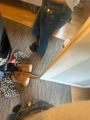 Mörkblå bootcut jeans från gina tricot - Säljer ett par mörkblå bootcut jeans med snygga guldknappar och klassiska fem fickor. Jeansen har låg midja och bootcut, perfekta för en avslappnad och trendig look. Materialet är denim med en lätt tvättad finish. 