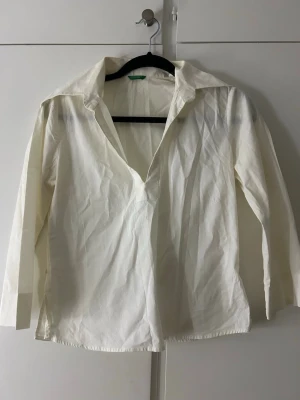 Vit långärmad henley-skjorta - Klassisk vit henley-skjorta med lång ärm och djup v-ringning. Skjortan har bred krage och är tillverkad i ett mjukt bomullstyg. Perfekt för en avslappnad men ändå stilren look. Storlek M en passar mer xs/s.