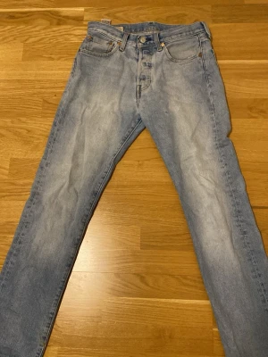Levi's  jeans - Säljer ett par ljusblå Levi's  jeans med klassisk stil och raka ben. Jeansen har en snygg tvättad look och är tillverkade i bomull med detaljer i kopparfärg. Perfekta för en avslappnad och trendig stil.