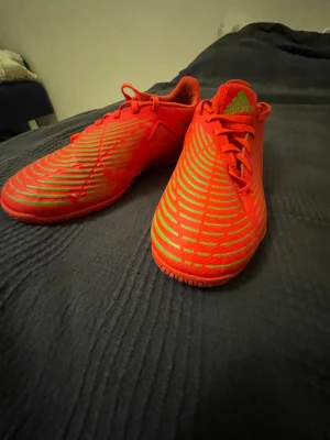 Röda Adidas sneakers med neonmönster - Säljer ett par riktigt snygga röda Adidas sneakers med neongröna detaljer och coolt mönster över hela skon. Skorna har lågt skaft, snörning och en slitstark sula med grepp. Perfekta för dig som vill sticka ut med färg och stil.