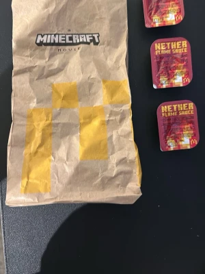 Minecraft x McDonald's Nether Flame Sauce. St pris - STYCKE PRIS. DE FÖRSTA SOM KÖPER EN FÅR PÅSEN. Unika Minecraft x McDonald's Nether Flame Sauce-dippar, 25 ml per förpackning. Medföljer även en brun papperspåse med Minecraft Movie-tryck och pixelgrafik i gult. Perfekt för samlare eller fans av Minecraft och McDonald's samarbeten.
