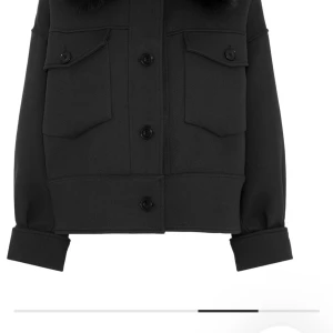 Meotine jacka - Snygg svart jacka med två stora bröstfickor och knappar framtill. Jackan har långärmade ärmar med breda muddar och en croppad passform som ger en cool vibe. Perfekt att slänga över en hoodie eller t-shirt för en chill look.