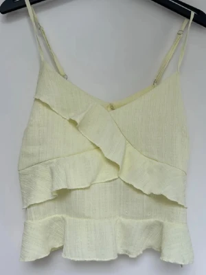 Ljusgul linnetopp med volanger - Supersöt ljusgul linnetopp med tunna axelband och volangdetaljer. 