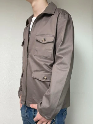Ijusbrun overshirt med fickor och dragkedja från John Henric  - Overshirt jacka från John Henric i en Ijusbrun färg. Modellen på bilden är 178 och väger ungefär 70kg och bär S/M. Hör gärna av er vid frågor eller funderingar!