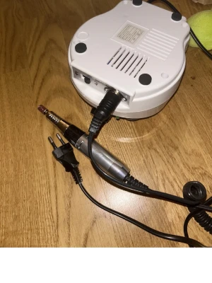 Elektrisk nagelfil Nail Drill vit - Elektrisk nagelfil från Nail Drill i vit plast med svart ratt och detaljer. Perfekt för att fila och forma naglar, både naturliga och konstgjorda. Utrustad med sladd och handstycke i silverfärg. Passar för både manikyr och pedikyr.