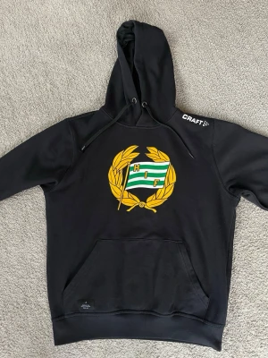 Hammarby IF hoodie, storlek S - Svart Bajen huvtröja med tryck framtill. Tröjan har en luva med dragsko och en känguruficka på magen. Muddar finns i ärmslut och nederkant.  Tröjan är använd men i fint skick.   Herrmodell, se mått på sista bilderna.