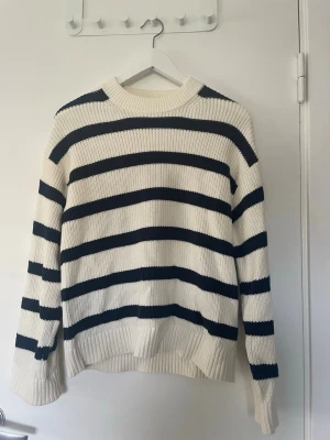 Vit stickad tröja med marinblå ränder - Säljer denna stickade tröja som är gammal och har tecken på användning, har några utdragna maskor här och var. 