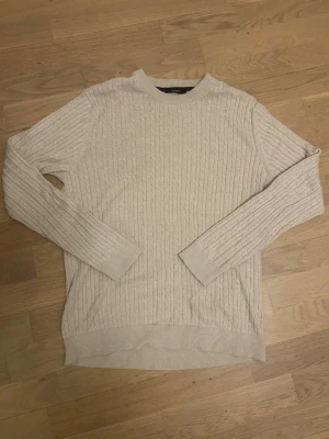Beige kabelstickad tröja Jack & Jones - Snygg beige kabelstickad tröja från Jack & Jones med rund halsringning och ribbade muddar. Tröjan har ett klassiskt mönster och är perfekt för lager på lager. Materialet känns mjukt och bekvämt, och färgen är lätt att matcha till olika outfits.