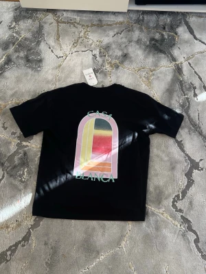 Casablanca t shirt - Svart t-shirt från Casablanca med färgglatt grafiskt tryck på både bröstet och ryggen. Trycket har en bågformad design i rosa, gul, röd och grön. T-shirten har normal passform och är tillverkad i mjuk bomull. Perfekt för dig som gillar streetwear och snygga prints.  Pris kan ev disskuteras, enbart seriösa köpare. Kan vid efterfrågan även mötas i Stockholm. Allt är i nyskick