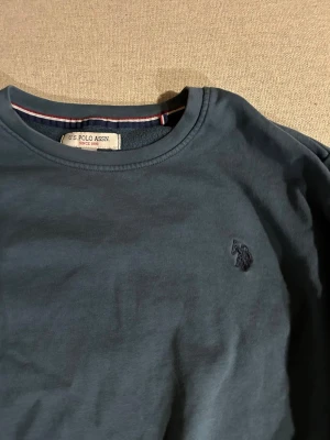 Mörkblå sweatshirt från US Polo Assn - Sweatshirt från US Polo Assn med rund halsringning och diskret broderad logga på bröstet. Tröjan har ribbade muddar vid ärmslut och nederkant. Perfekt för en avslappnad och stilren look.