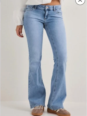 Bootcut jeans i ljusblå denim - Säljer ett par snygga bootcut jeans i ljusblå denim med klassisk femficksmodell och normal midja. Jeansen har utsvängda ben och stängs med knapp och dragkedja. Perfekta för en avslappnad och trendig look.