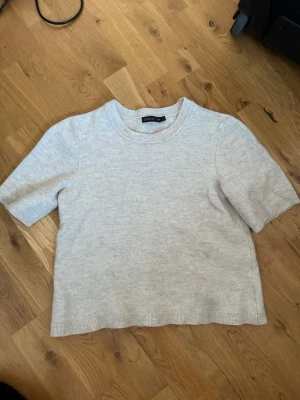 Ljusgrå stickad topp från Stockh lm - En enkel och stilren ljusgrå stickad topp från Stockh lm (MQ). Modellen har rund halsringning, korta ärmar och rak passform. Perfekt att matcha med jeans eller kjol för en clean look.