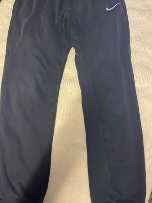 Mörkblå Nike mjukisbyxor - Snygga mörkblå mjukisbyxor från Nike med klassisk vit logga på höften. Byxorna har raka ben och resår i midjan. Perfekta för en avslappnad stil och tillverkade i mjukt material för extra komfort.