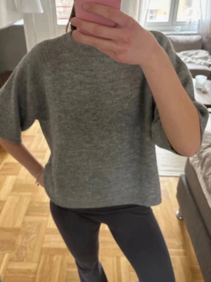 Grå oversized stickad tröja - Mysig grå stickad tröja med oversized passform och korta ärmar. Tröjan har en rund halsringning och är tillverkad i ett mjukt material som passar perfekt för lager på lager. Enkel och stilren design som funkar till det mesta.