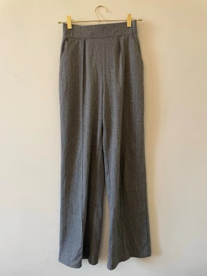 Grå kostymbyxor med hög midja - Snygga grå kostymbyxor med diskreta kritstreck, hög midja och raka ben. Byxorna har pressveck framtill och sidfickor. Perfekta för en clean och stilren look. Materialet känns mjukt och har en klassisk kostymkänsla.
