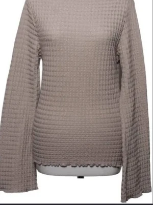 Beige ribbad topp med vida ärmar - Trendig beige topp med ribbad struktur och vida långärmar. Toppen har en lätt vågig kant nedtill och är perfekt för dig som gillar en stilren men ändå unik look. Passar till både jeans och kjol.