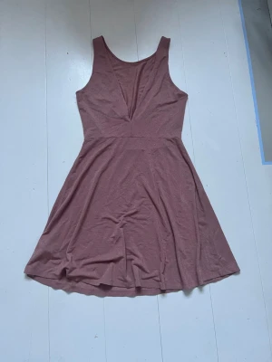 Rosa kortklänning med v-ringning - Säljer en enkel och snygg rosa kortklänning med v-ringad front och ärmlös design. Klänningen har en lätt utställd kjol och är tillverkad i ett mjukt material som känns bekvämt mot huden. Perfekt för varma dagar eller när du vill känna dig extra fin.