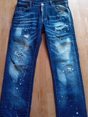 Dsquared - Säljer ett par blå jeans från Ciao Bella med slitna detaljer, färgstänk och tryck på bakfickan. Jeansen har raka ben, fem fickor och coola slitningar framtill. Perfekta för dig som gillar en streetwear-look.