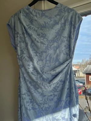 Ljusblå spetsklänning med öppen rygg - Snygg ljusblå kortklänning med blommigt spetsmönster och öppen rygg. Klänningen har en figurnära passform och är ärmlös, perfekt för sommarens alla tillfällen.☀️