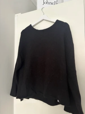 Svart stickad tröja med öppen rygg - Mysig svart stickad tröja med rund halsringning fram och stor, djup urringning i ryggen. Tröjan har lång ärm och en något lös passform. 