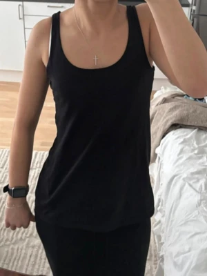 Svart linnetopp med breda axelband - En enkel och stilren svart linnetopp med breda axelband och rundad urringning. Perfekt att matcha med jeans eller kjol för en clean look. Materialet känns mjukt och följsamt mot kroppen.