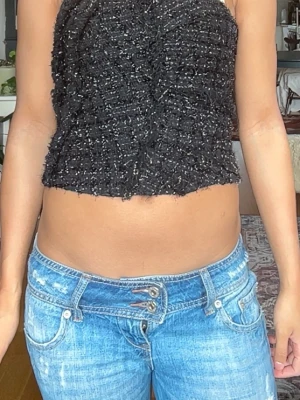 Svart croppad topp i bouclé - Säljer en svart croppad topp i bouclé-liknande material med glittriga inslag. Toppen är ärmlös och har en tight passform som framhäver midjan. Perfekt för dig som vill ha en trendig och unik topp till din garderob.