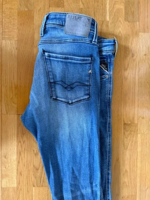 Blå jeans från Replay - Säljer ett par snygga blå jeans från Replay med klassisk femficksdesign och ljus tvätt. Jeansen har raka ben, tydliga sömmar på bakfickorna och Replay-logga på bakre linningen. Perfekta för en avslappnad och trendig look.