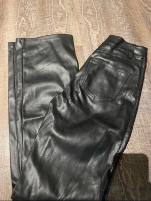 Svarta jeans i skinnimitation - Snygga svarta jeans i skinnimitation med klassisk femficksdesign och raka ben. Materialet är mjukt och har en matt finish, insidan är fodrad för extra komfort. Perfekta för dig som vill ha en edgy look.