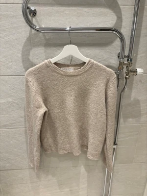 Beige stickad tröja från Pull&Bear - Mysig beige stickad tröja från Pull&Bear med rund halsringning och långa ärmar. Tröjan har en enkel och stilren design med ribbade muddar vid ärmslut och nederkant. Perfekt för lager-på-lager och chill dagar.