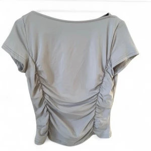 Beige topp med rynkade sidor - Snygg beige topp med korta ärmar och rynkade sidor som ger en cool och trendig look. Perfekt att styla med jeans eller kjol för en avslappnad vibe. Materialet känns mjukt och bekvämt mot huden.