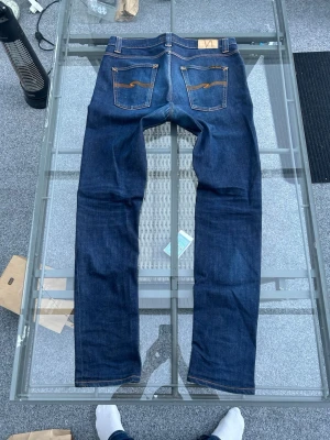 Nudie Jeans Lean Dean – Dry 16 Dips, W33 L34 - Säljer mina Nudie Jeans i modellen Lean Dean, en av deras mest uppskattade modeller. Jeansen kommer i den mörka och tidlösa tvätten "Dry 16 Dips".  Modell: Lean Dean (slim fit med avsmalnande ben).  Storlek: W33 L34.  Material: 99 % ekologisk bomull och 1 % elastan för perfekt passform.  Skick: Mycket fint skick. En stilren klassiker i hållbar kvalitet som passar perfekt till allt. Skriv gärna om du har några frågor eller vill ha fler bilder! 