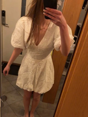 Vit kort klänning  - Superfin vit kort klänning från Bubbleroom med broderat blommönster, puffärmar och v-ringning. Klänningen har även ett knytband i midjan som man själv kan justera! Endast använd 1 gång. Nypris 899 kr. 