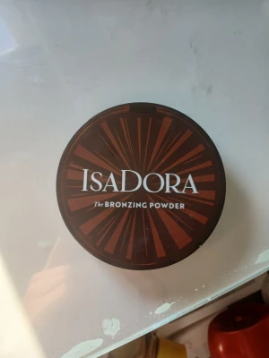 Isadora Bronzing Powder brun - Snygg bronzer från Isadora i en rund brun plastförpackning med spegel i locket. Ger en naturlig solkysst look med sin varma bruna nyans. Perfekt för att framhäva ansiktskonturer och ge glow till huden.