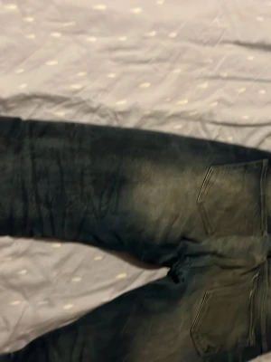 Mörkblå raka jeans med slitningar - Säljer ett par mörkblå jeans med raka ben och snygga slitningar. Jeansen har två bakfickor och klassisk femficksdesign. Materialet är denim i bomull och de har en tvättad look som ger en cool vibe.