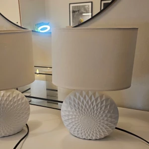 2st Cottex Amadeus vita bordslampor - Säljer 2 st Cottex Amadeus stilren vit bordslampa med rund, geometriskt mönstrad fot i keramik och enkel lampskärm i tyg. Lampan har en modern design som passar perfekt på nattduksbord eller i vardagsrummet. Sladd med strömbrytare ingår. MEN skärmarna har fått lite slag , kunde ej ladda upp alla bilder här men kan skicka om nån vill. Annars är de bara köpa nya lampskärmar - för lampfoten är super snygg!!