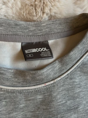 Grå sweatshirt från 32 Degrees Cool - Mjuk och enkel grå sweatshirt från 32 Degrees Cool. Tröjan har rund halsringning, långa ärmar och diskreta vita sömmar vid muddar och hals. Perfekt för en avslappnad och stilren look.