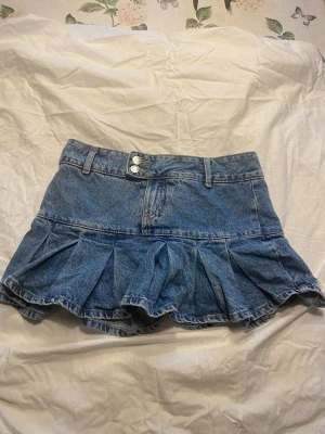 Jeanskjol med volang från Bershka - Snygg blå jeanskjol från Bershka med volang nertill och dubbla knappar i midjan. Kjolen har klassisk denimlook och bälteshällor.