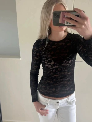 Svart spetsig långärmad topp - Säljer en svart långärmad topp i spets med transparenta partier. Toppen har en tight passform och rund halsringning. Perfekt att styla med jeans eller kjol för en trendig look.