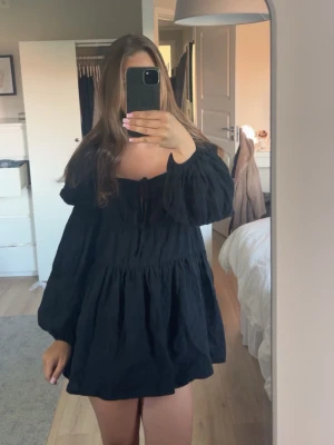 Svart kort klänning med puffärm - Supersöt svart kort klänning med puffiga långärmar och offshoulder-modell. Klänningen har en lätt volangig kjol och knytning framtill vid bysten. Perfekt för dig som gillar en avslappnad men ändå trendig stil. den är från ”In the style” och har aldrig använt den. 