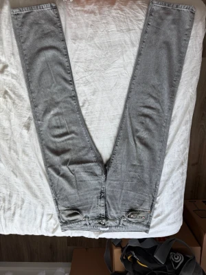 Gråa slim fit jeans från Woodbird - Snygga gråa slim fit jeans från Woodbird med klassisk femficksdesign och diskreta slitningar. Jeansen har en rak passform och är tillverkade i mjukt denimtyg med stretch för extra komfort. Perfekta för en trendig och avslappnad look.
