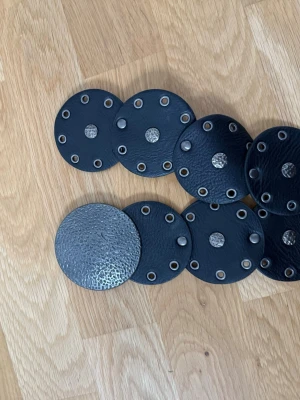 Svart cirkelformat skärp i skinn - Unikt Coachella inspirerat svart skärp med stora runda cirklar i skinn och metallnitar. Skärpet har en boho-vibe och passar perfekt för att ge outfiten en cool touch. Snygg detalj till kjol eller klänning och justerbart i midjan.