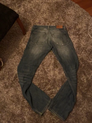 Acne blå slim fit jeans - Säljer ett par blå Acne jeans med slitningar och raka ben. Jeansen har klassisk femficksdesign och ljus tvätt med tydliga slitdetaljer framtill och baktill. Ny pris: 2899.