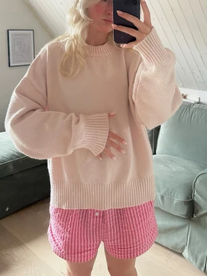 Ljusrosa oversized stickad tröja - Supermjuk och oversized stickad tröja i ljusrosa med breda ribbade muddar vid ärmslut och nederkant. Tröjan har rund halsringning och en relaxed fit som ger en chill och trendig look. Perfekt för lager på lager under hösten eller en sen sommarkväll.
