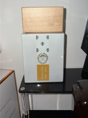 Bianco Oro parfym 100 ml - Exklusiv parfym från Giardino Benessere i en stilren vit flaska med trälock. Flaskan har guldiga och svarta detaljer samt en etikett med texten 'Bianco Oro'. Volymen är 100 ml och designen känns både modern och lyxig.