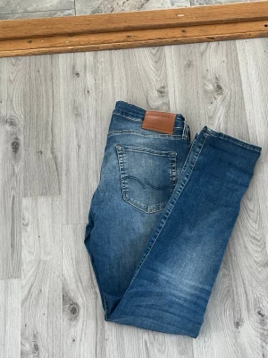 Blå jeans från Jack & jones - Säljer ett par klassiska blå jeans från Jack and Jones Jeans med fem fickor och snygga slitningar. Jeansen har en rak passform och är gjorda i denim med en cool tvätt. Perfekta för dig som gillar en avslappnad men stilren look.