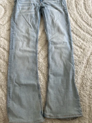Ljusblå bootcut jeans från weekday  - Säljer ett par ljusblå bootcut jeans i klassisk denim med fem fickor och knappgylf. Jeansen har en avslappnad passform och lätt utsvängda ben, perfekta för en trendig och avslappnad look. Och är uppsydda