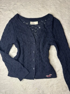 Hollister vintage kofta - Snygg marinblå kofta från Hollister! Väldigt eftertraktad och svår att få tag på! Snyggt hålmönstrar och sitter fint på. Lite korta vid ärmarna då modellen är så!