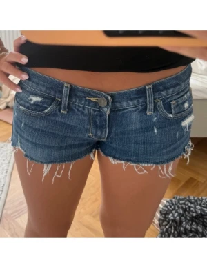 Blå lågmidjaze jeansshorts - Säljer ett par super snygga mörkblå jeansshorts, dom är väldigt Lågmidjade och har en fransig kant längst ner