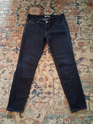 Mörkblå slim jeans - Säljer ett par mörkblå slim jeans med klassisk femficksdesign och smala ben. Jeansen har silverfärgade nitar och knapp, samt kontrastsömmar. Perfekta för dig som gillar en enkel och stilren look. Pris kan diskuteras och fråga om funderingar 